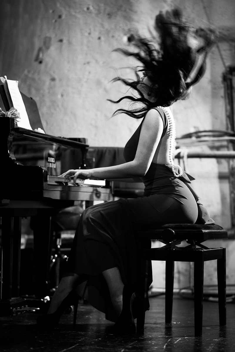 Black and white portrait of a pianist seen from behind, her hair flying as she plays
