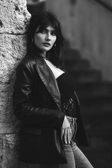 Black and white portrait of a woman in a leather jacket leaning on the wall of a staircase