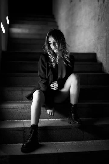 Black and white portrait of a woman in a black coat sitting on a dark staircase