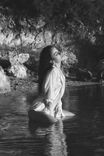 Black and white portrait of a woman in a white shirt in the water among the rocks, her face to the sky