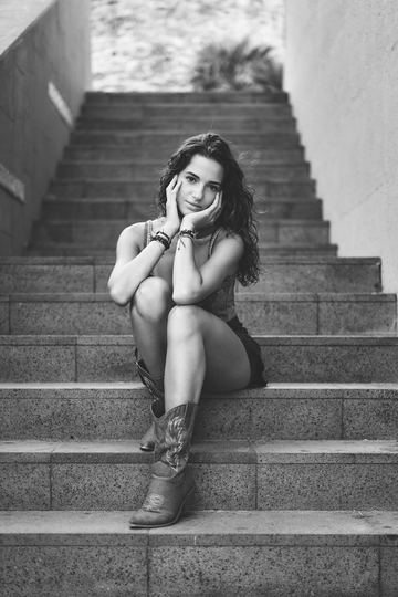Black and white portrait of a woman sitting on a staircase in boots, her hand on her face
