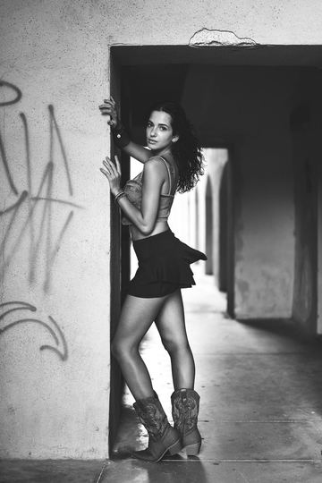 Black and white portrait of a woman in cowboy boots in a doorway with graffiti