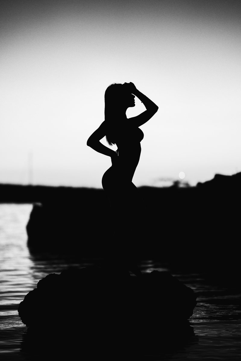 Black and white silhouette of a woman against the light by the sea, at sunset