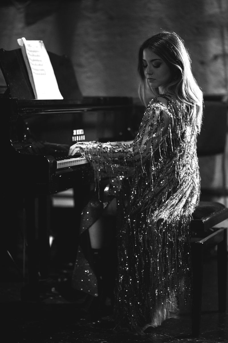 Ritratto in bianco e nero di una donna in cardigan di paillettes seduta al pianoforte, di tre quarti