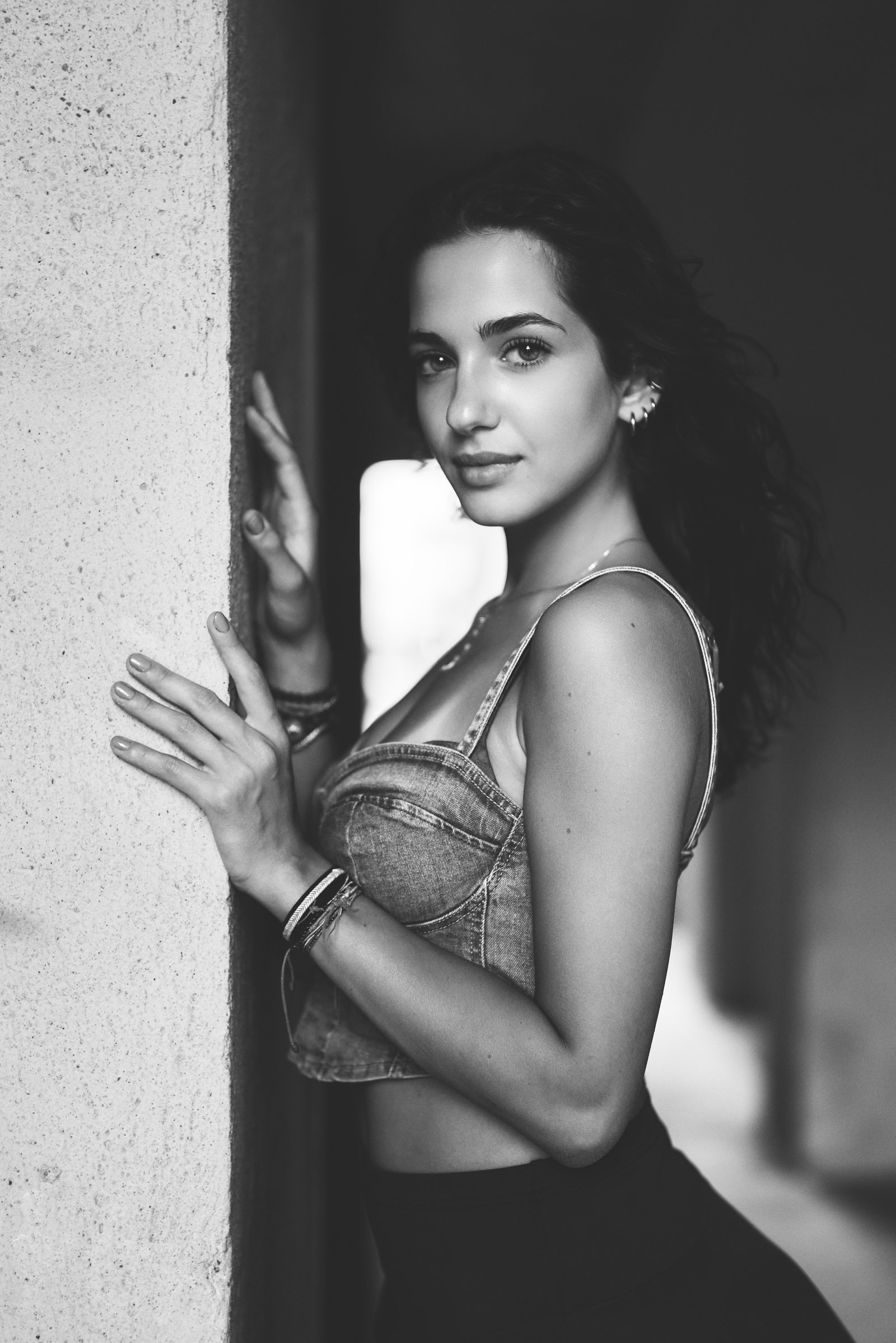 Black and white portrait of a woman leaning against a wall, her hand on it, looking into the camera