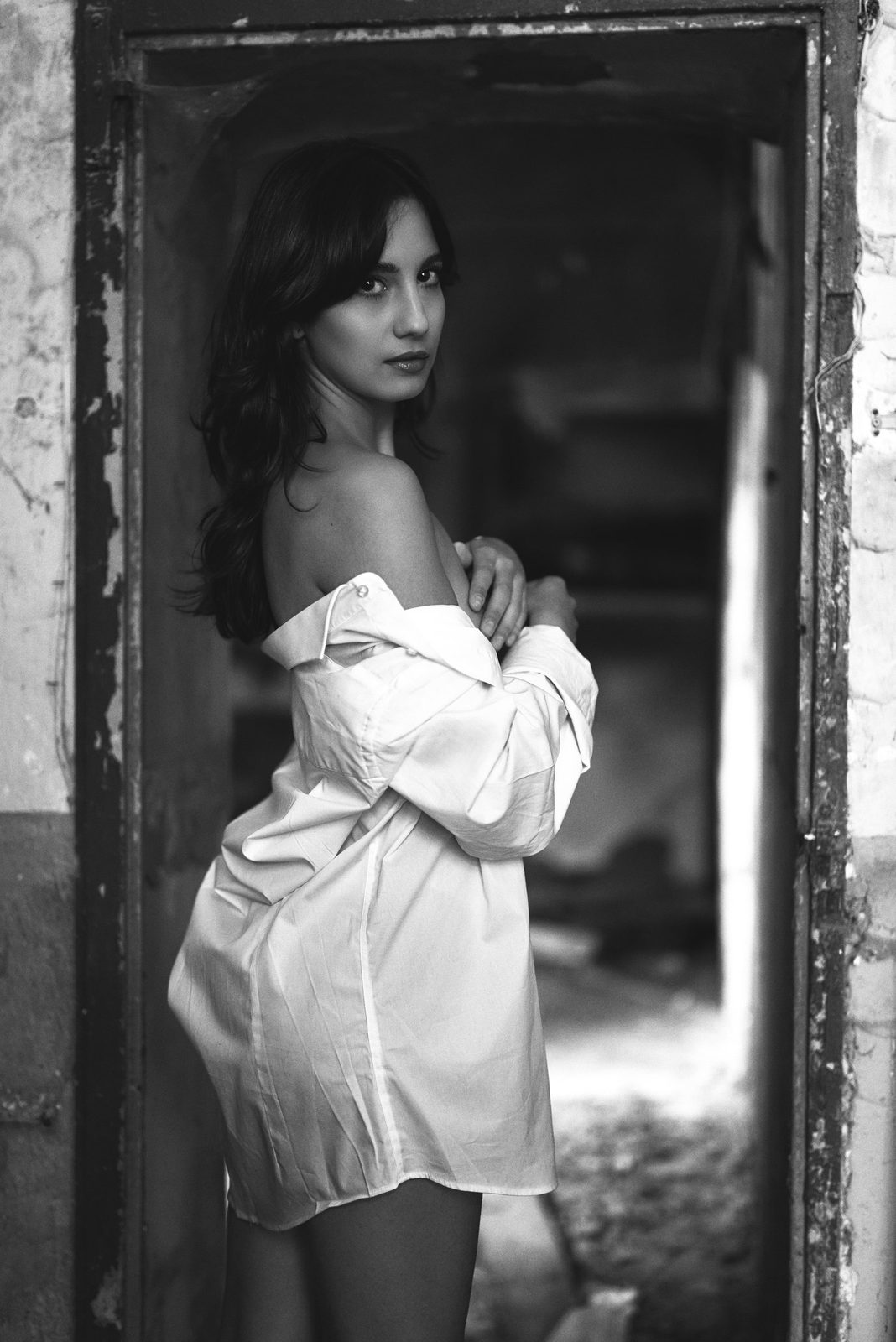 Ritratto in bianco e nero di una donna in camicia bianca sulla soglia di una porta