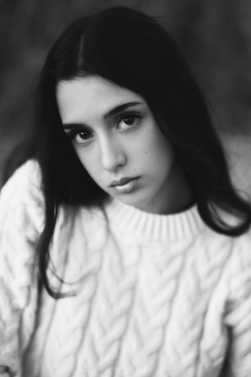Ritratto in bianco e nero di una ragazza con i capelli scuri e un maglione bianco a trecce, lo sguardo in camera