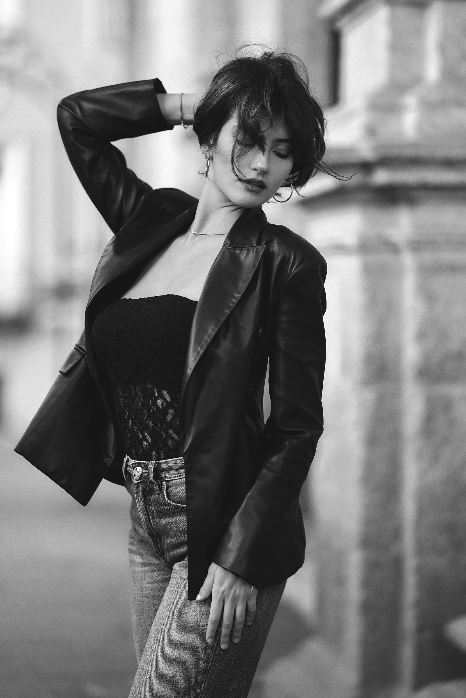 Ritratto in bianco e nero di una donna in giacca di pelle, la mano tra i capelli, in una piazza