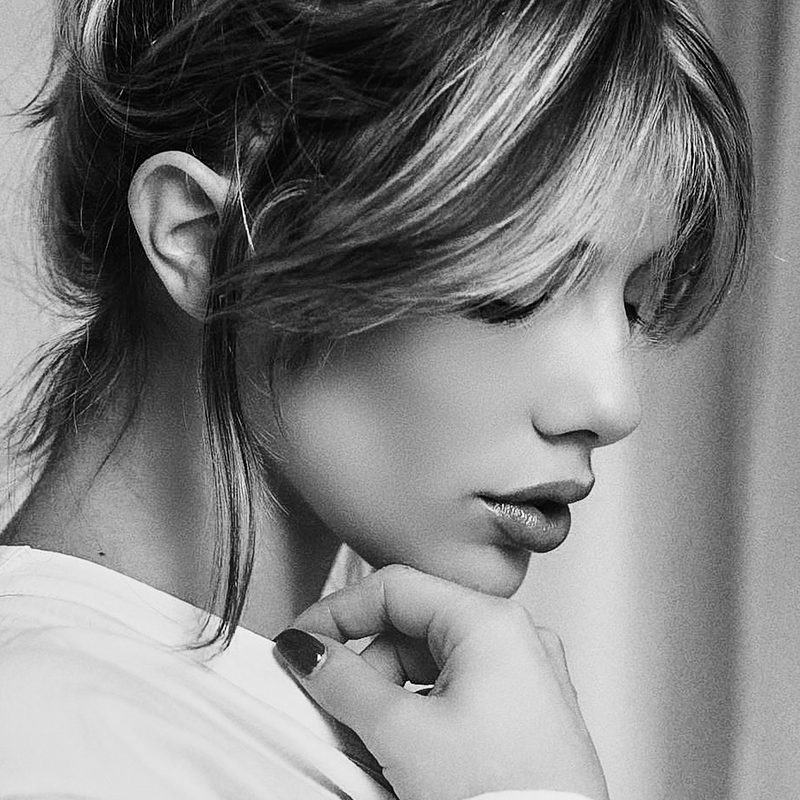 Ritratto in bianco e nero di una giovane donna di profilo, con la frangia e la mano al mento, luce di finestra