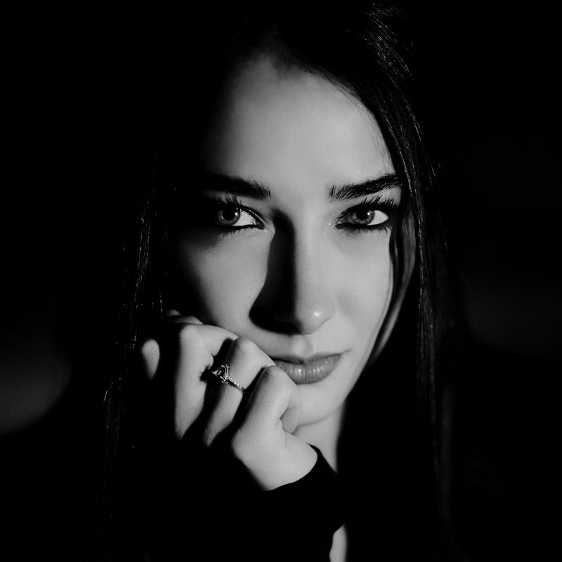 Ritratto in bianco e nero di una donna a mezza luce, con l'anello alla mano, sfondo scuro