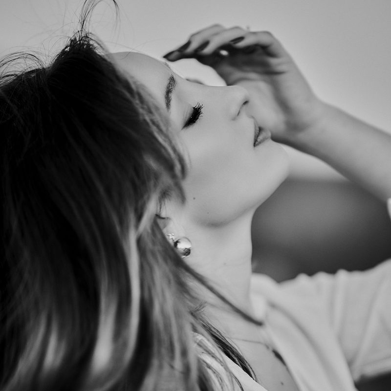 Ritratto in bianco e nero di una donna con il viso rivolto verso la luce, una mano tra i capelli