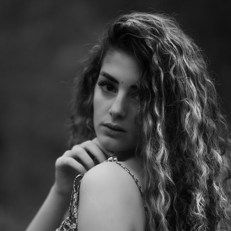 Ritratto in bianco e nero di una donna con i capelli ricci, di spalle, lo sguardo oltre la spalla