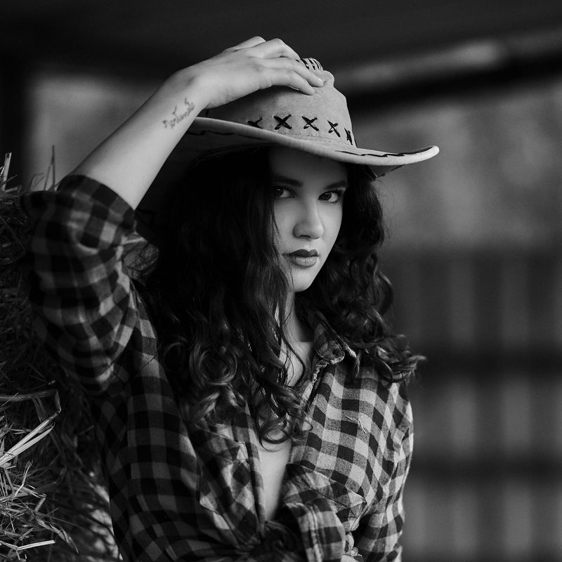 Ritratto in bianco e nero di una donna con un cappello di paglia e la camicia a quadri, in campagna