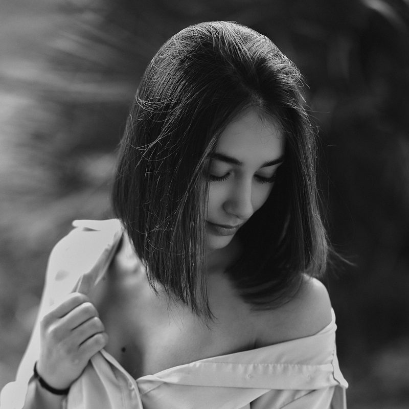 Ritratto in bianco e nero di una donna con i capelli corti che guarda verso il basso, in un giardino