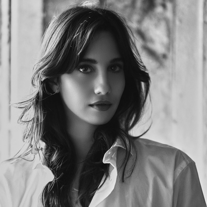 Primo piano in bianco e nero di una donna con lo sguardo diretto e un sorriso appena accennato