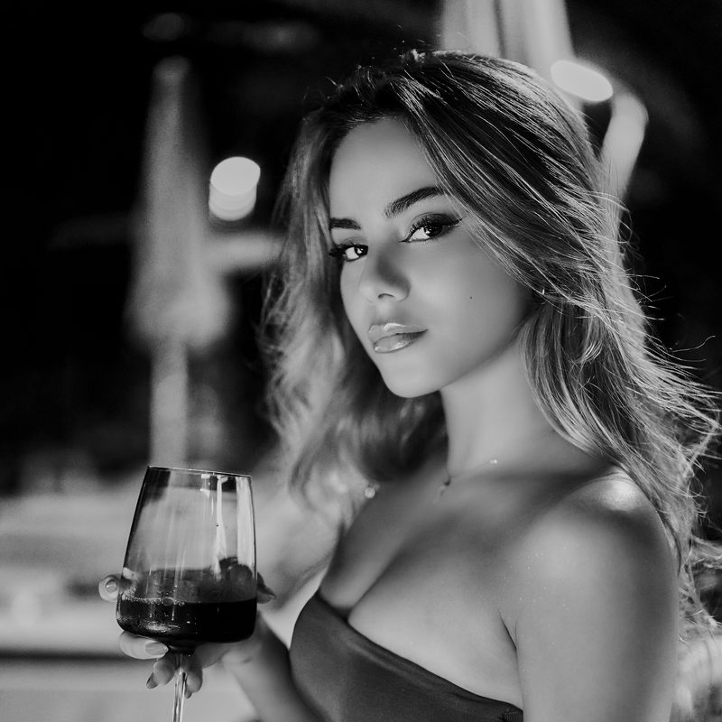 Ritratto in bianco e nero di una donna con gli occhiali, la mano al mento, sfondo scuro