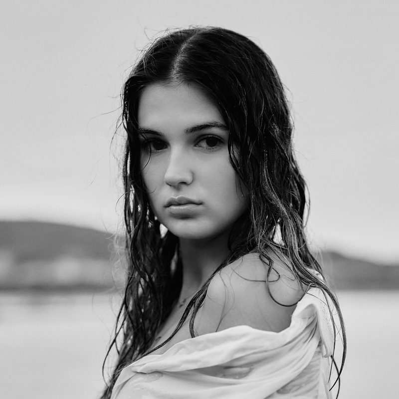 Ritratto in bianco e nero di una donna in camicia bianca con i capelli bagnati, davanti al mare
