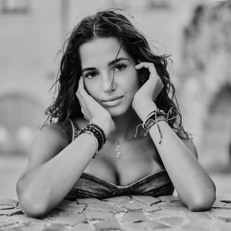 Ritratto in bianco e nero di una donna in camicia nera, lo sguardo abbassato, contro un muro