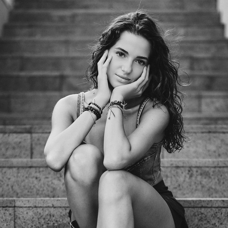 Ritratto in bianco e nero di una donna con le mani sul viso e i bracciali, in riva al mare