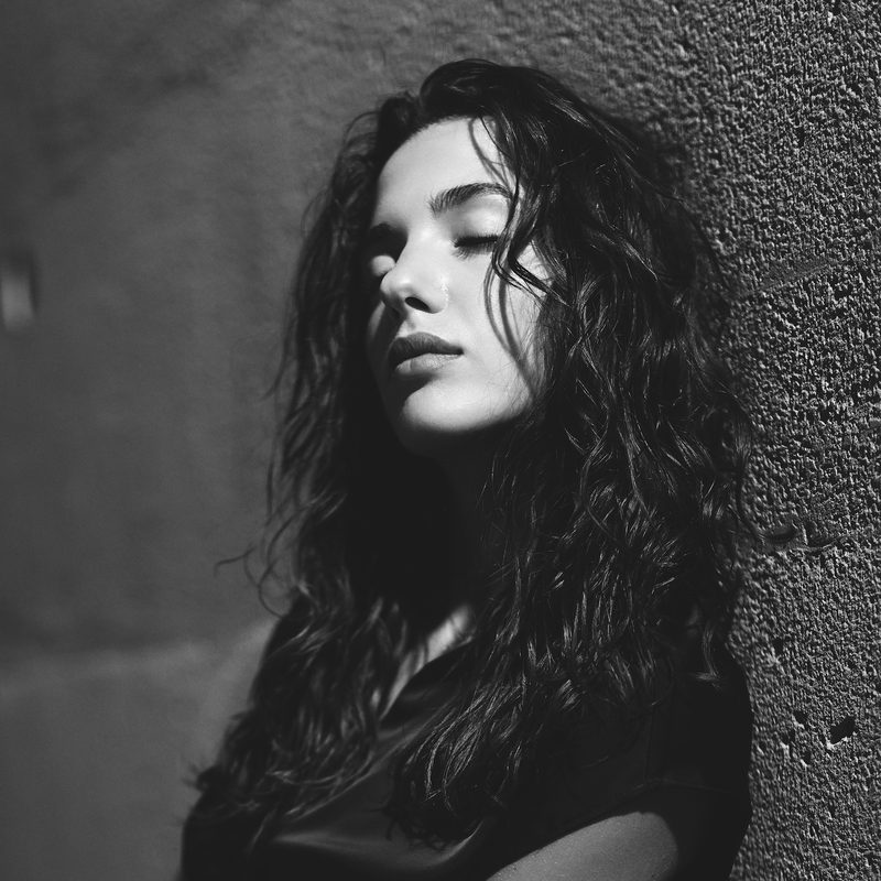 Ritratto in bianco e nero di una donna in un vicolo, la mano appoggiata al muro