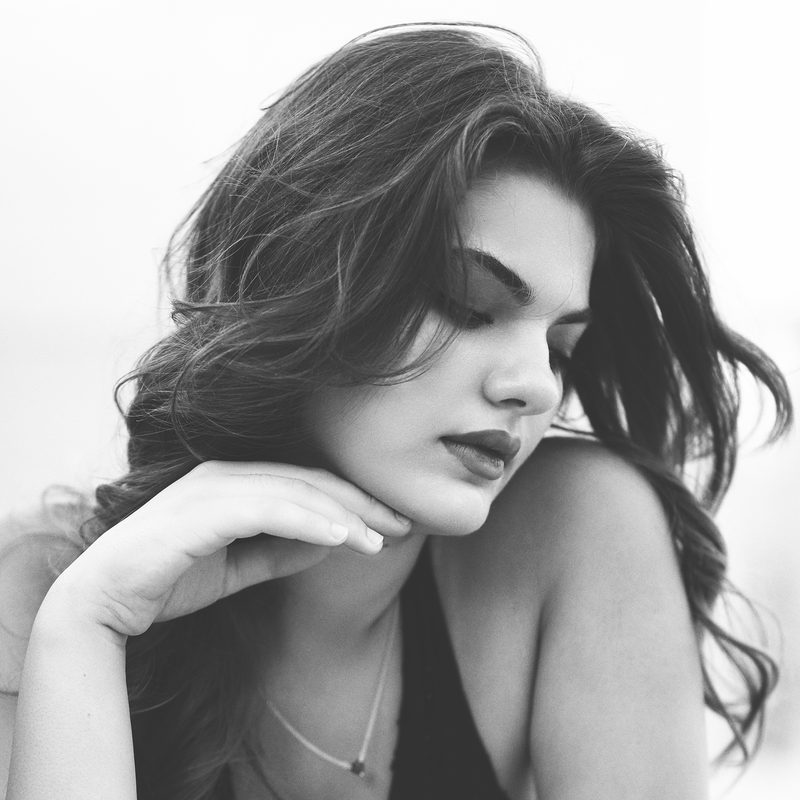Ritratto in bianco e nero di una donna con i capelli ricci, gli occhi chiusi, contro un muro