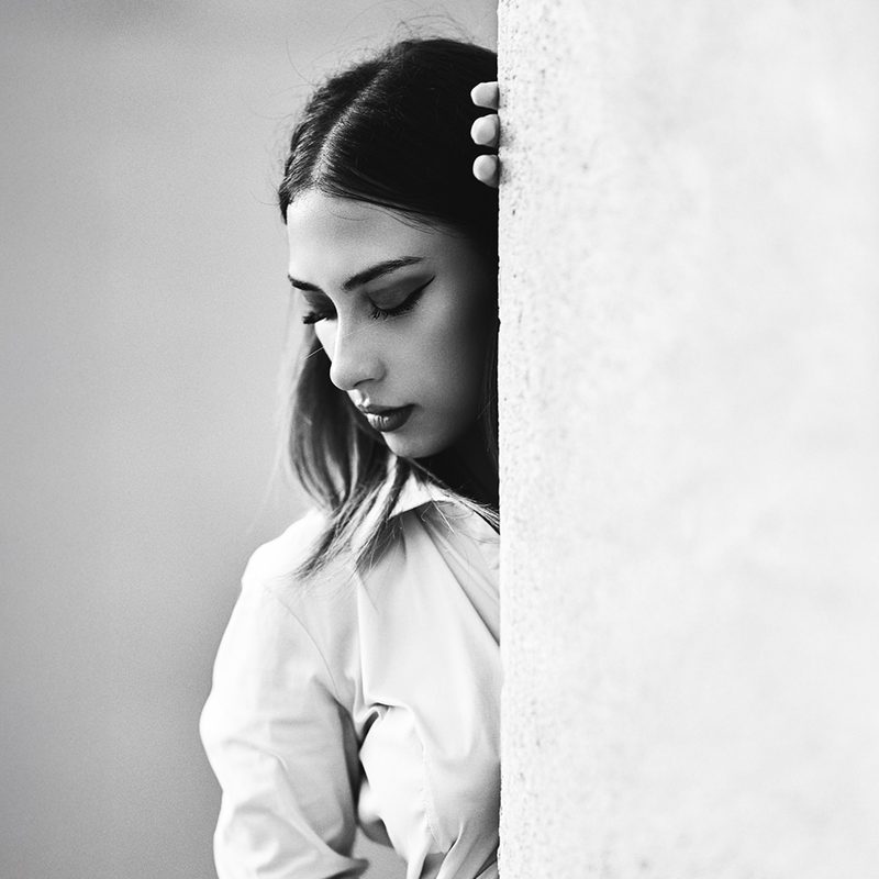 Ritratto in bianco e nero di una donna in camicia bianca appoggiata a una colonna